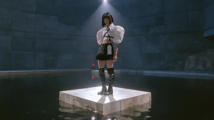 a young woman with a glossy black blunt bob with heavy bangs and one clay-orange streak, a white cropped puff-sleeve shirt, a black pleated skirt with a harness belt and a hanging white garment tag, black knee-high…