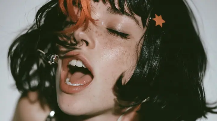 close-up in three-quarter profile of a young Caucasian American woman with pale skin and light freckles, a glossy black blunt jaw-length bob with heavy bangs and one clay-orange streak through the bangs, a small flat…