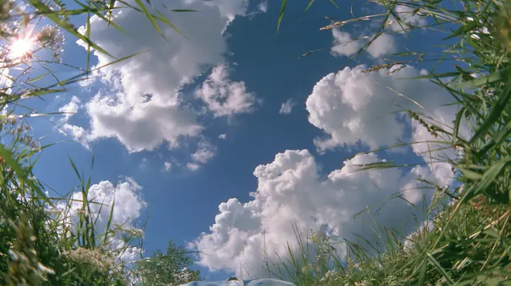 Y2K high fashion editorial photograph, 2001: first-person view lying on your back in the grass looking straight up at a deep blue sky with soft white cumulus clouds, grass blades at the edges of frame, bright sun, no…