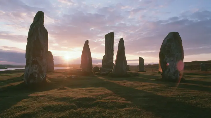 Y2K high fashion editorial photograph, 2001: a luxury campaign landscape of ancient standing stones silhouetted against a glowing violet and amber sunset, medium-format slide film, no text, no letters, no logos
