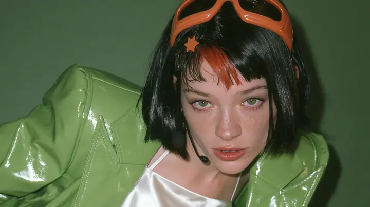 Y2K high fashion editorial, 2001: a medium close-up of a Caucasian American woman in her mid-twenties with pale skin and light freckles, a glossy black blunt jaw-length bob with heavy straight bangs and one…