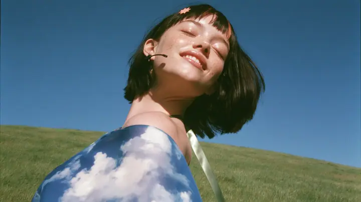 Y2K high fashion editorial, 2001: a medium shot of a Caucasian American woman in her mid-twenties with pale skin and light freckles, a glossy black blunt jaw-length bob with heavy straight bangs and one clay-orange…